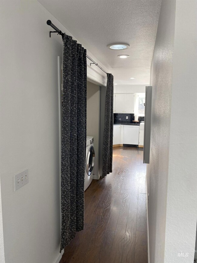 Hall featuring a textured ceiling, dark wood-style floors, a textured wall, and washer / clothes dryer