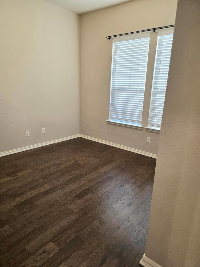 Empty room featuring baseboards and dark wood finished floors