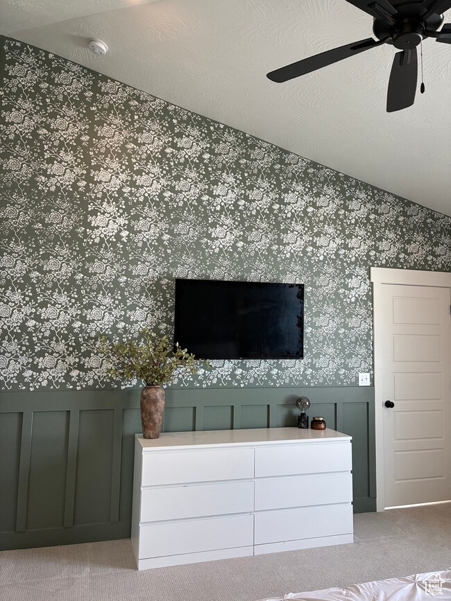 Unfurnished bedroom featuring carpet floors, wallpapered walls, a wainscoted wall, ceiling fan, and a decorative wall