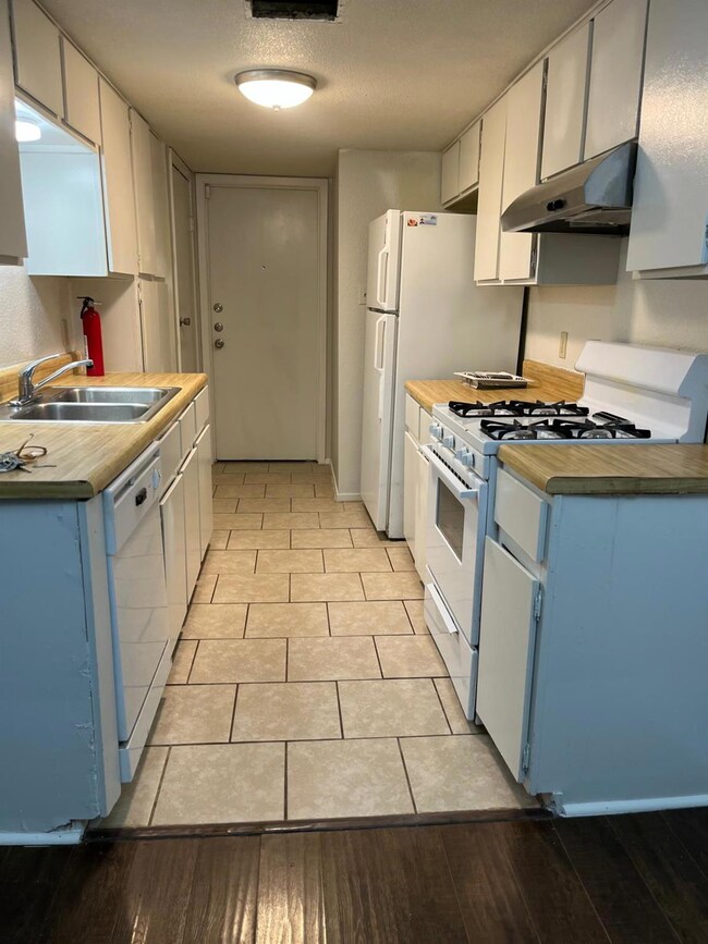 Kitchen with white appliances, under cabinet range hood, butcher block countertops, and blue cabinetry