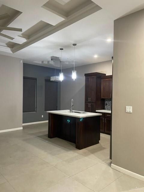 Kitchen featuring sink, dark brown cabinets, a center island with sink, pendant lighting, and backsplash