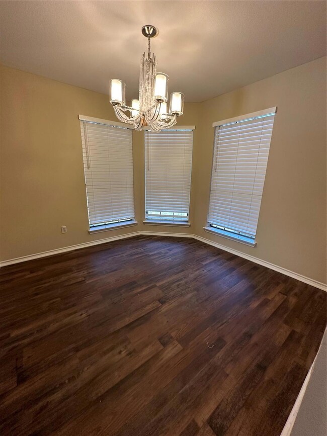 Empty room featuring dark hardwood / wood-style floors and an inviting chandelier