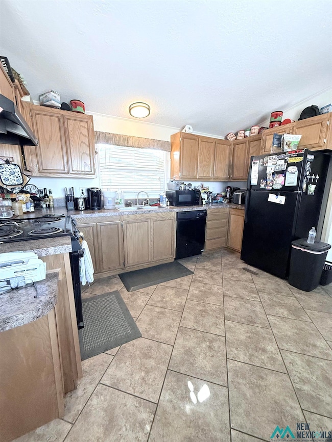Kitchen featuring black appliances, under cabinet range hood, light tile patterned flooring, light countertops, and brown cabinets