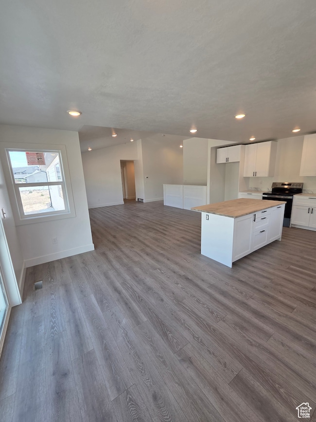 Kitchen with electric stove, open floor plan, dark wood-style flooring, butcher block counters, and white cabinetry