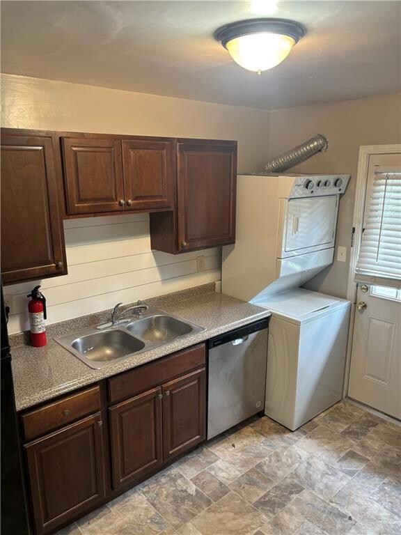 Kitchen with stainless steel dishwasher, stacked washer / drying machine, dark brown cabinets, and stone finish floors