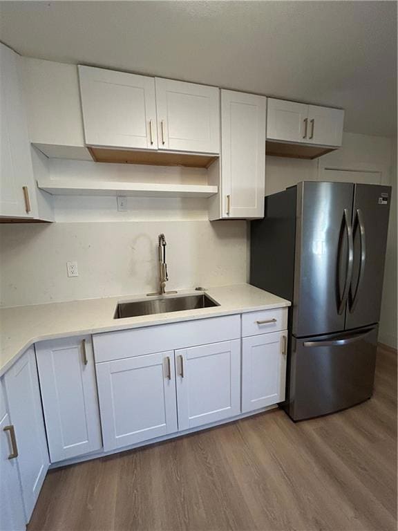 Kitchen with fridge, white cabinetry, light wood finished floors, and light stone counters