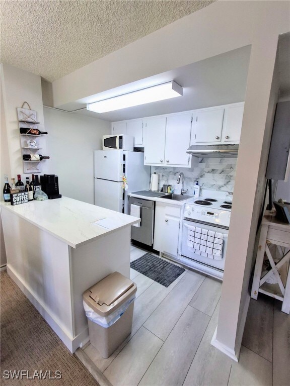 Kitchen featuring white appliances, under cabinet range hood, white cabinetry, backsplash, and light wood finished floors