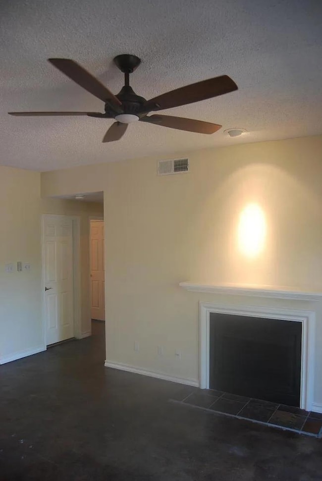 Unfurnished living room featuring a textured ceiling, ceiling fan, and a tiled fireplace
