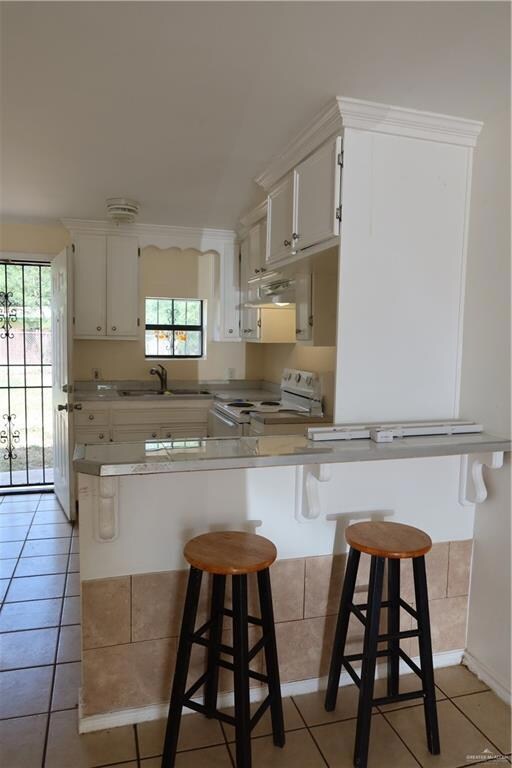 Kitchen featuring range, light tile patterned floors, and a kitchen breakfast bar