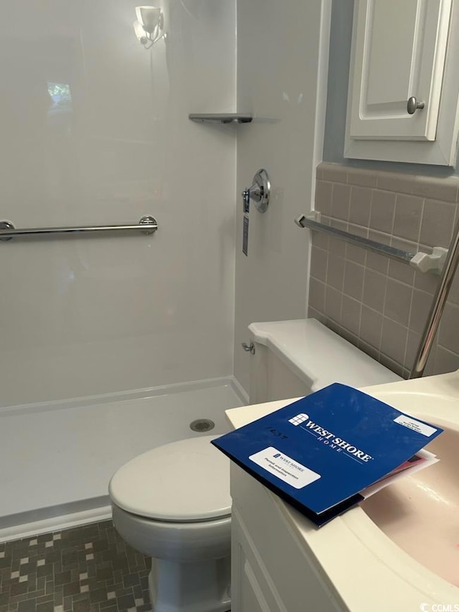 Bathroom featuring vanity, toilet, and a shower
