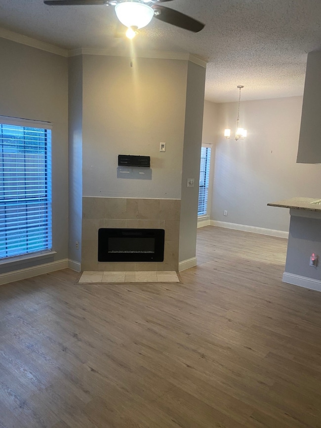 Unfurnished living room with light wood-style flooring, a textured ceiling, a tile fireplace, ceiling fan, and a chandelier