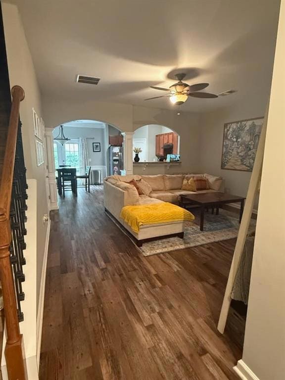 Living area with arched walkways, decorative columns, a ceiling fan, dark wood-style floors, and stairway