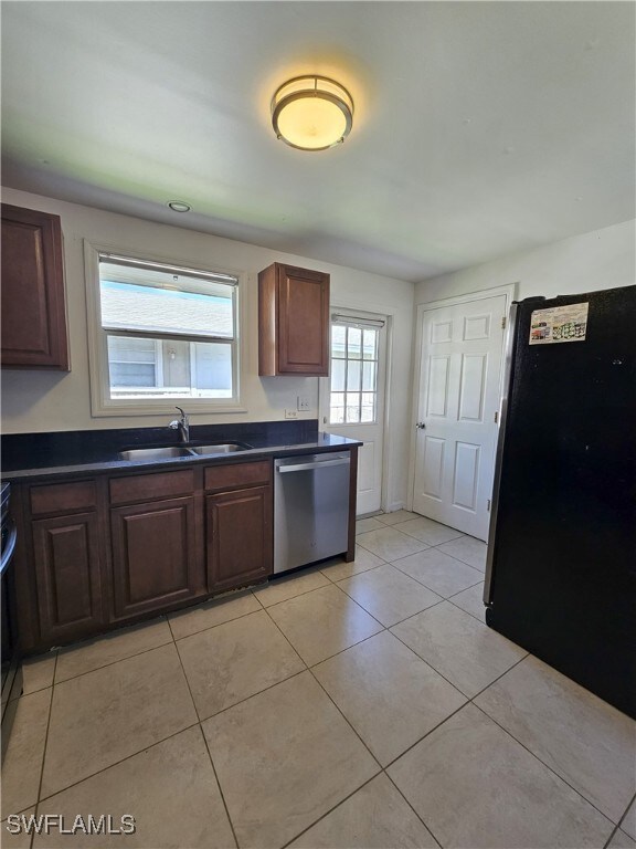 Kitchen featuring freestanding refrigerator, dark countertops, stainless steel dishwasher, and light tile patterned flooring