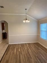 Unfurnished dining area featuring ornamental molding, dark wood-style flooring, vaulted ceiling, arched walkways, and a chandelier