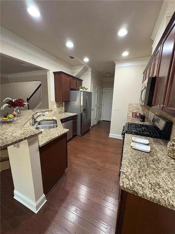 Kitchen with appliances with stainless steel finishes, crown molding, a peninsula, decorative backsplash, and light stone counters
