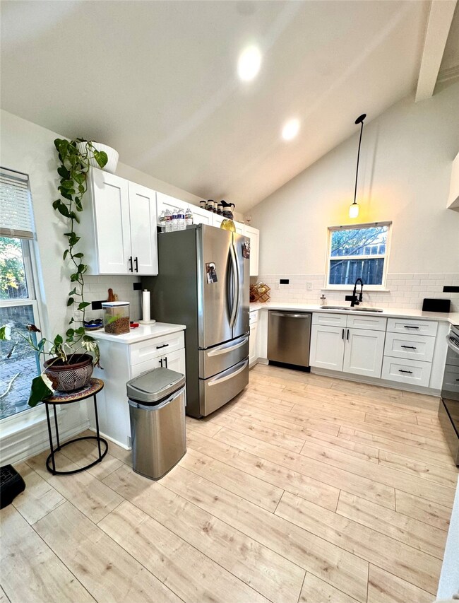 Kitchen with lofted ceiling, white cabinetry, tasteful backsplash, stainless steel appliances, and decorative light fixtures