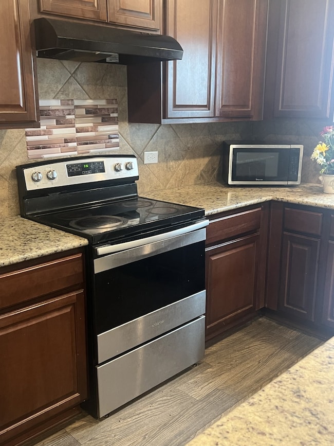 Kitchen featuring appliances with stainless steel finishes, under cabinet range hood, and tasteful backsplash