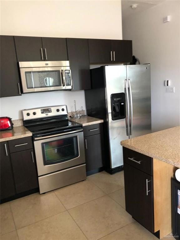 Kitchen with light tile patterned floors, appliances with stainless steel finishes, dark cabinets, and light countertops