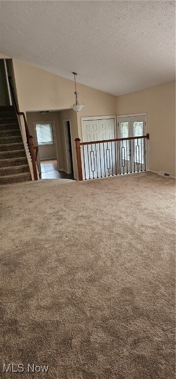 Carpeted empty room featuring a textured ceiling and vaulted ceiling