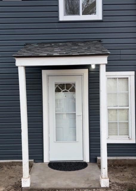 View of exterior entry with a shingled roof