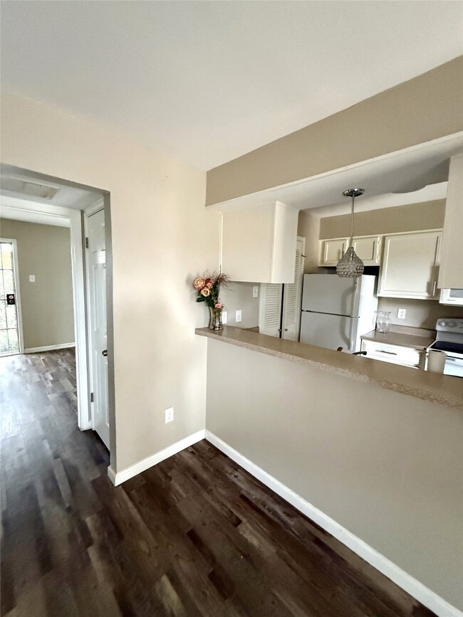 Kitchen with white cabinetry, white appliances, light countertops, and dark laminate flooring