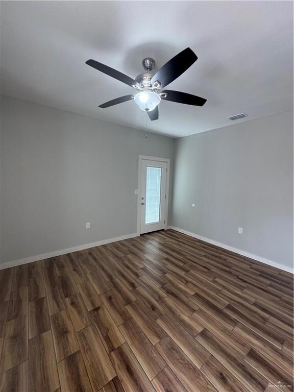 Unfurnished room with dark wood finished floors, baseboards, visible vents, and ceiling fan