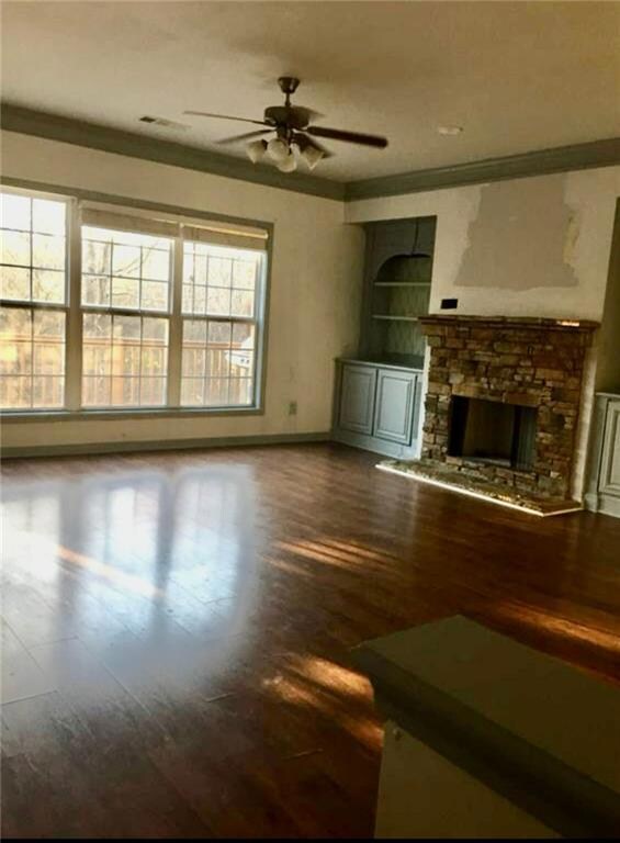 Unfurnished living room with wood finished floors, ceiling fan, a fireplace, built in features, and crown molding