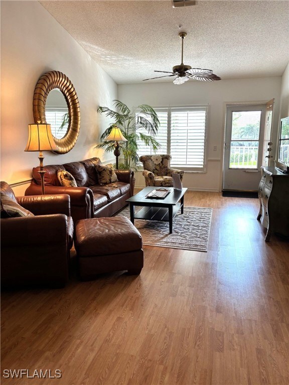 Living room with a textured ceiling, wood finished floors, and ceiling fan