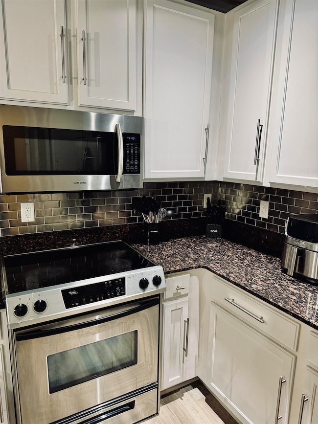 Kitchen featuring appliances with stainless steel finishes, white cabinets, dark stone counters, and backsplash