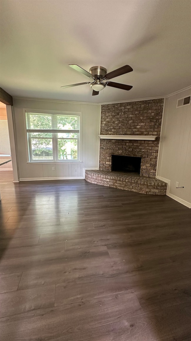 Unfurnished living room featuring a ceiling fan, dark wood-style flooring, a brick fireplace, and crown molding