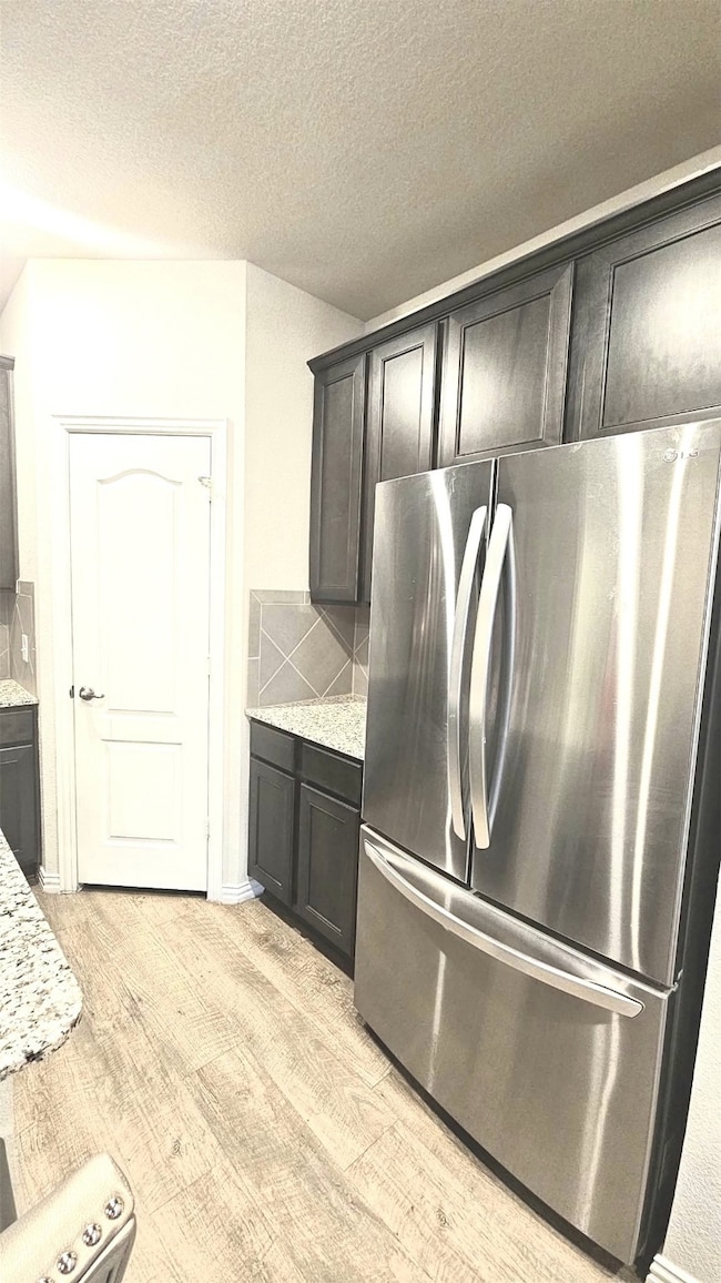 Kitchen with freestanding refrigerator, light wood-style flooring, light stone countertops, decorative backsplash, and a textured ceiling