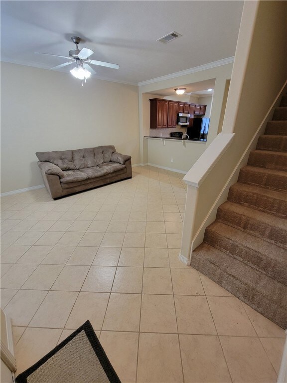 Living room with ornamental molding, light tile patterned floors, ceiling fan, and stairway