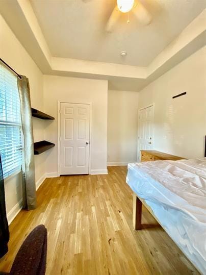 Bedroom with a raised ceiling, light wood-type flooring, and ceiling fan