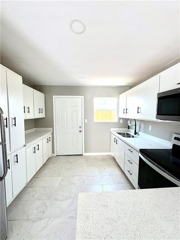 Kitchen featuring stainless steel appliances, white cabinetry, light countertops, and light marble finish floors