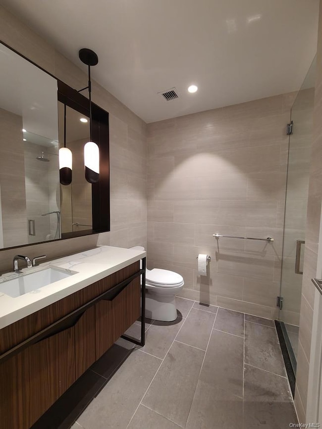 Bathroom featuring tile walls, a stall shower, vanity, recessed lighting, and light tile patterned floors