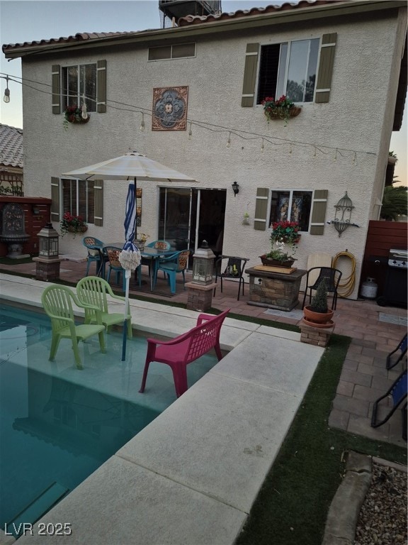 Rear view of house with a patio area, stucco siding, a tiled roof, and an outdoor pool