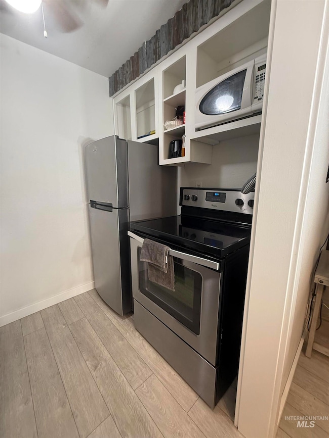 Kitchen featuring stainless steel appliances, light wood-style floors, white cabinetry, ceiling fan, and glass insert cabinets