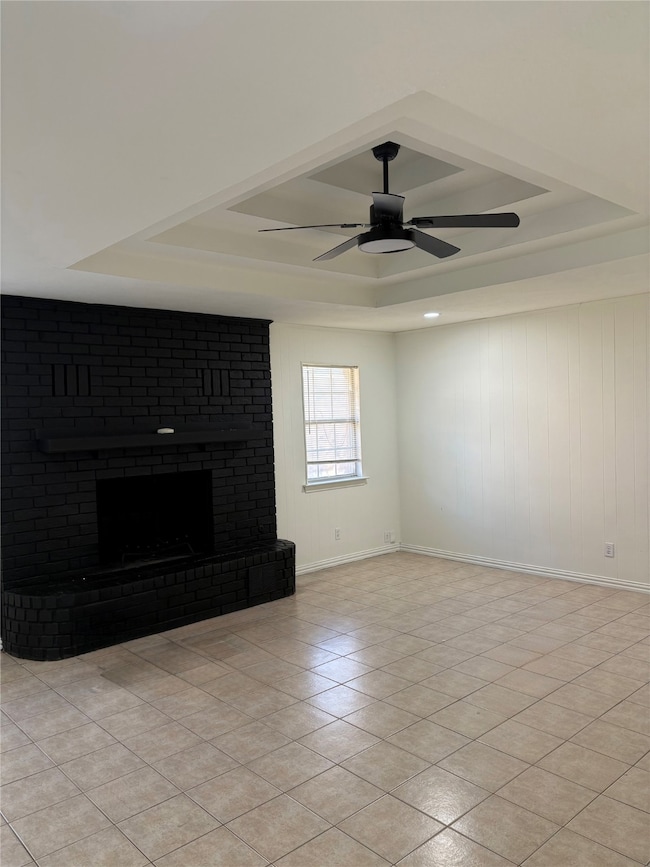 Unfurnished living room with a tray ceiling, a brick fireplace, wood walls, and light tile patterned floors
