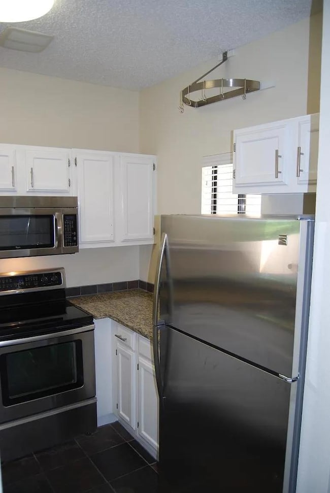 Kitchen with appliances with stainless steel finishes, white cabinets, a textured ceiling, dark tile patterned floors, and dark stone counters