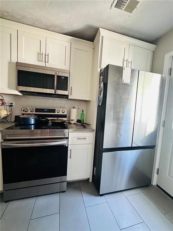 Kitchen featuring stainless steel appliances, decorative backsplash, white cabinets, light tile patterned floors, and a textured ceiling