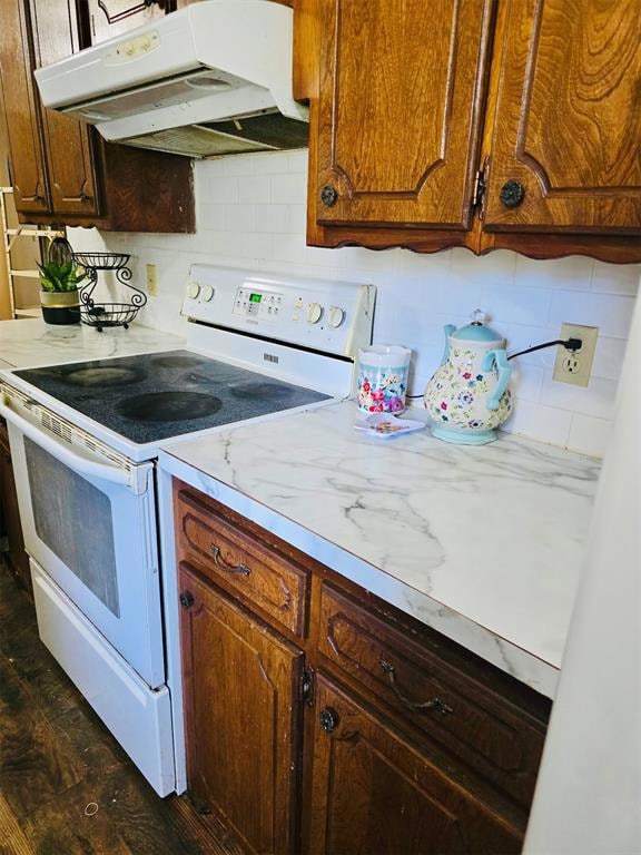 Kitchen with white electric range, tasteful backsplash, under cabinet range hood, light countertops, and dark wood-style floors