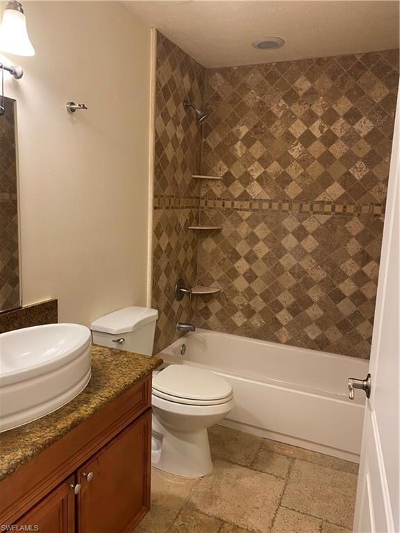 Bathroom featuring vanity, bathing tub / shower combination, stone tile floors, and toilet
