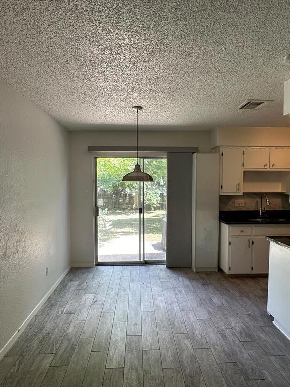 Unfurnished dining area featuring a textured wall, light wood-style floors, and a textured ceiling
