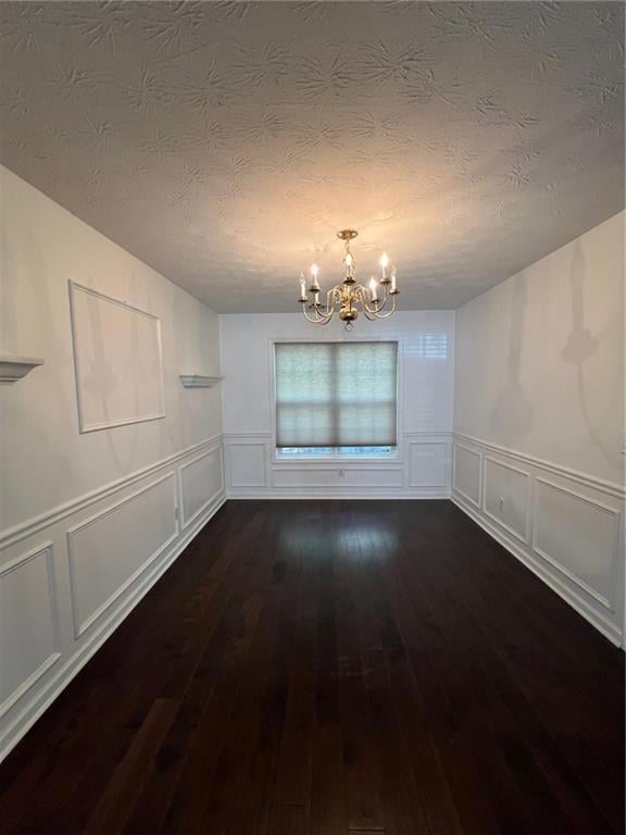 Unfurnished dining area featuring a chandelier, a textured ceiling, and dark wood-style flooring
