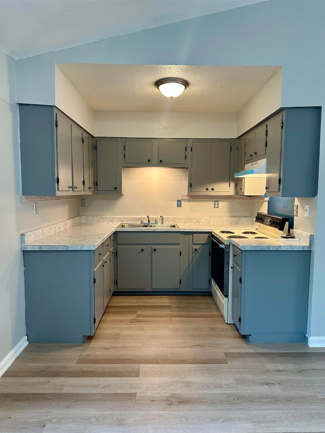 Kitchen featuring white electric range oven, under cabinet range hood, a sink, light wood-style floors, and a textured ceiling