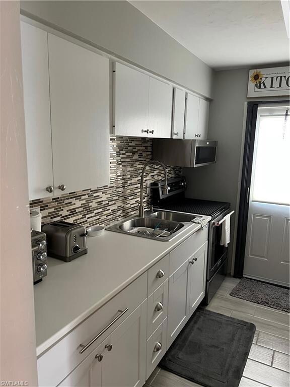 Kitchen featuring range, backsplash, a sink, white cabinets, and light countertops