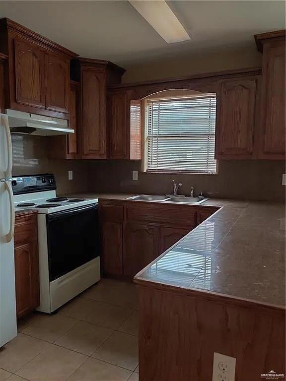 Kitchen with under cabinet range hood, a sink, light tile patterned floors, and white appliances