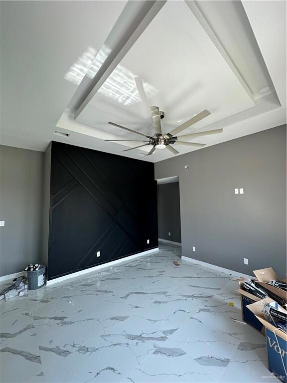 Spare room with a tray ceiling, ceiling fan, and tile floors