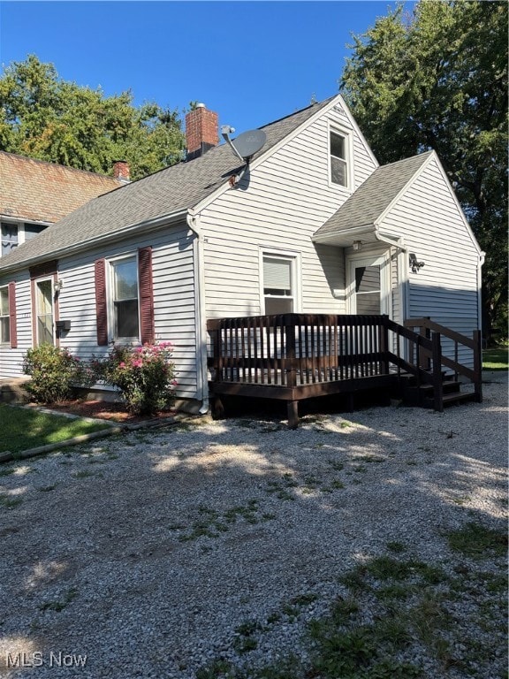 Back of property featuring a shingled roof, a wooden deck, and a chimney