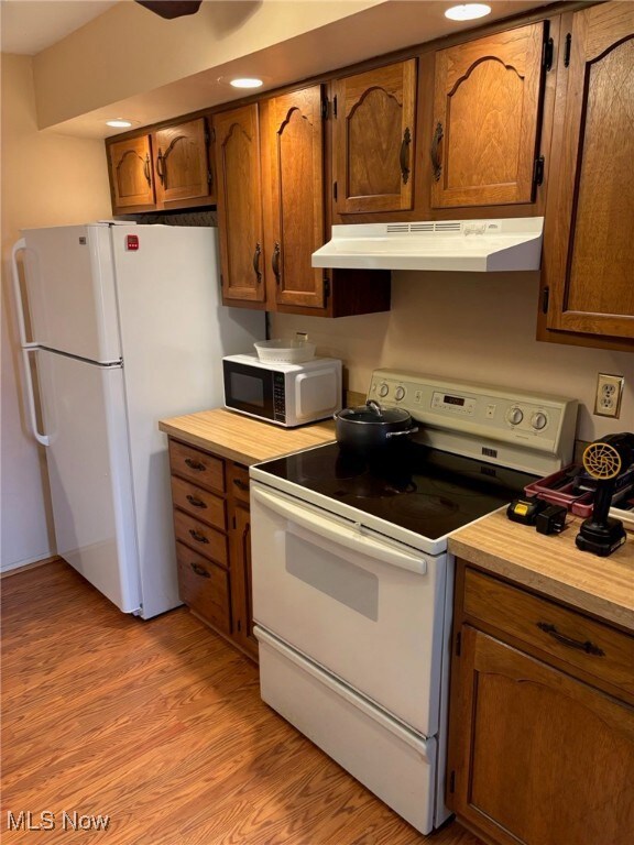 Kitchen featuring white appliances, light countertops, light wood-style flooring, brown cabinets, and under cabinet range hood